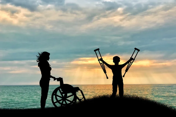 Παιδί με ειδικές ανάγκες με πατερίτσες δίπλα σε αναπηρικό καροτσάκι και νοσοκόμα στην παραλία — Φωτογραφία Αρχείου