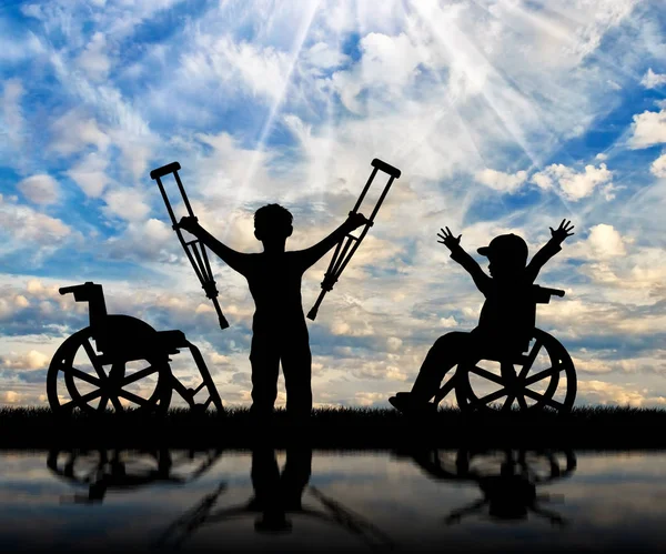 Мальчик в инвалидном кресле и мальчик-инвалид, стоящий с костылями день — стоковое фото