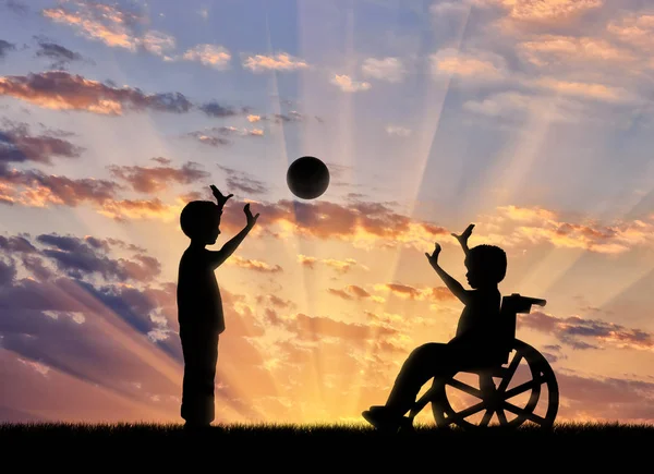 Menino feliz em uma cadeira de rodas brincando com um menino por do sol — Fotografia de Stock