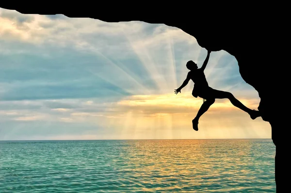 Альпинист взбирается на скалу над закатом моря — стоковое фото