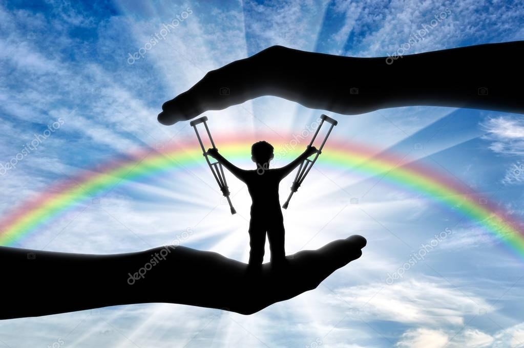 Child disabled person with crutches in hand on background rainbow day