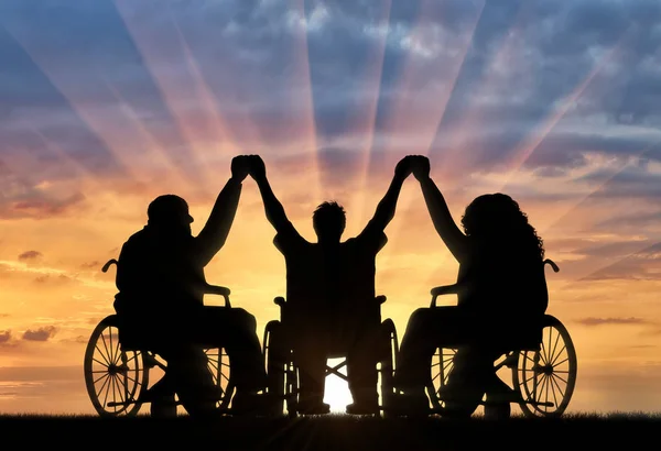 Инвалиды в инвалидных колясках держатся за руки на закате — стоковое фото