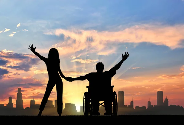 Инвалид в инвалидной коляске с подружкой на фоне города — стоковое фото