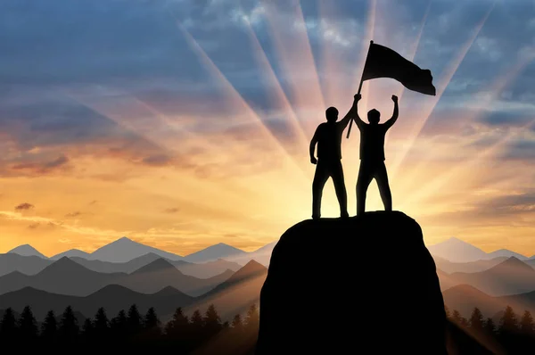 Sylwetka dwóch wspinaczy na szczycie góry z flagą w ręku — Zdjęcie stockowe