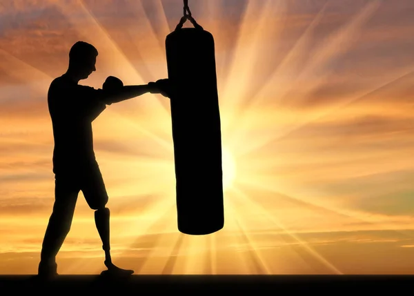 Silhouette of a disabled man with a leg prosthesis, training with a punching bag