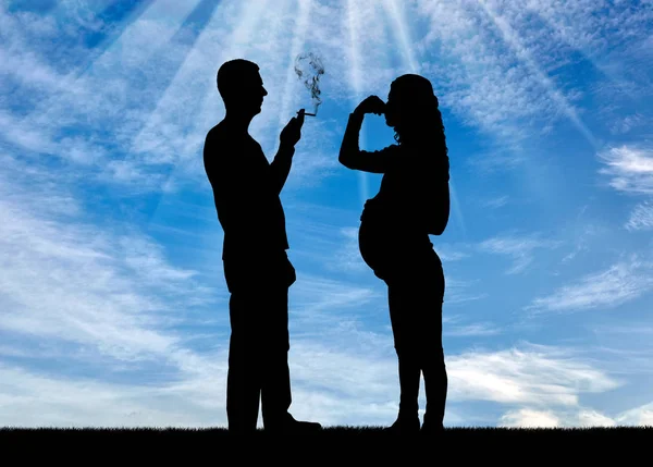 Силуэт мужчины-эгоиста, курящего возле беременной женщины. Она закрыла нос рукой от дыма. — стоковое фото