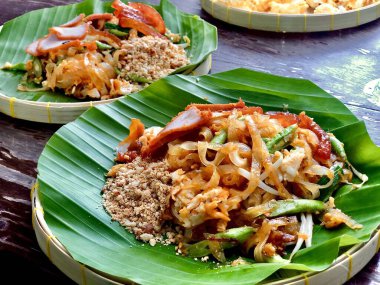 Pad Thai, Tayland yemeği ünlü erişteli kızarmış yumurta, domuz eti, uzun fasulye ve fıstık ile Tayland usulü restoranda muz yaprağı tabağı ve bambu tepsisi üzerine konmuş lezzetli baharatlı tatlı tadı olan.