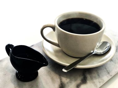 Koyu kahve, beyaz seramik bardakta olmayan amerikan içkisi, siyah küçük sürahiyle şurubu granit tepsi dikdörtgen şeklinde metal kaşıkla yerleştirilmiş, sabahları tazeliği hisseden, kopyalama alanı var..