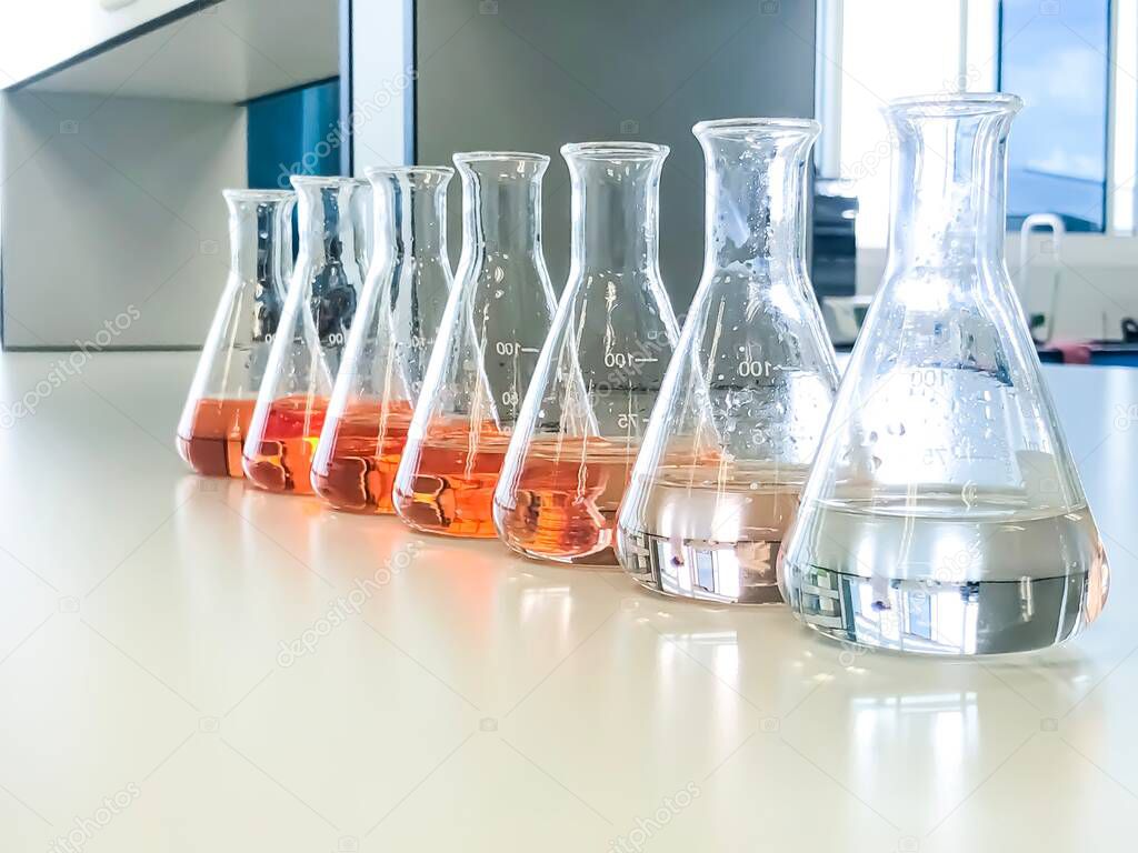 The Erlenmeyer or Conical flask on bench laboratory, with gradient solvent for analysis concentration range of iron show the orange color compound, detect with UV-spectrophotometer in waste water.
