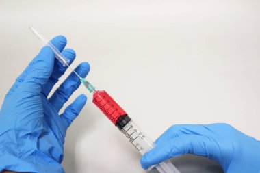 Bilimadamları, cam şişeye kırmızı çözeltileri aktarmak için şırınga kullanarak kimyasal aşıyı test eden mavi nitril eldivenler giyiyorlar..