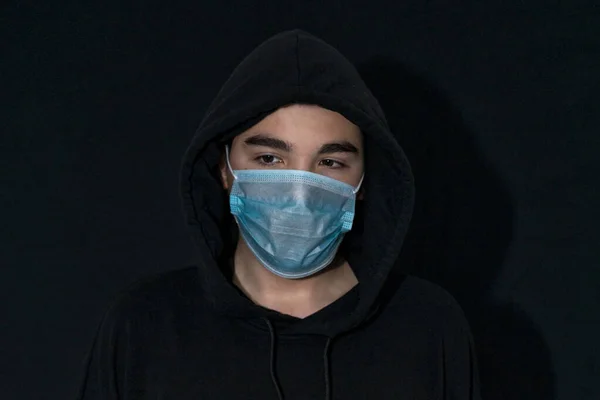 teenager in a black hood and a disposable mask in the dark. Coronavirus 2019