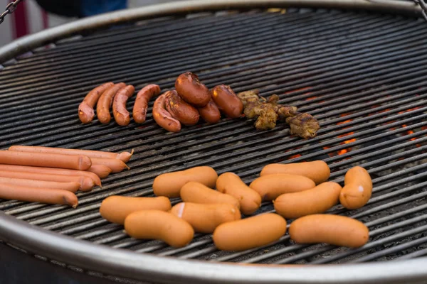 delicious thick and thin sausages are grilled on a round grill on a street party.