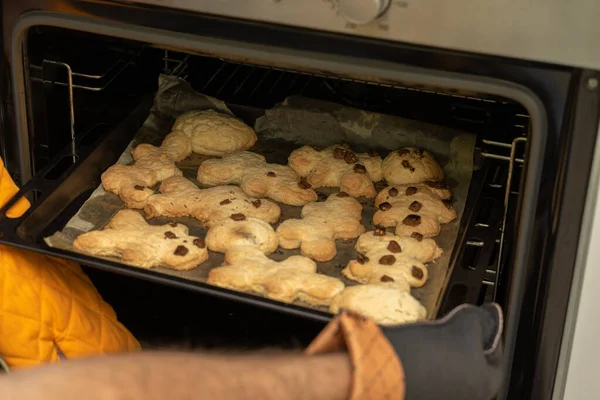 a hand in a kitchen glove takes out tasty oven cookies in the shape of men from the oven