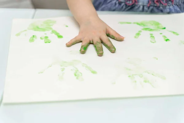 Little girl paints with fingers.a child s hand in green paint is on a white sheet of paper, self-isolation, coronavirus covid-19, stay home