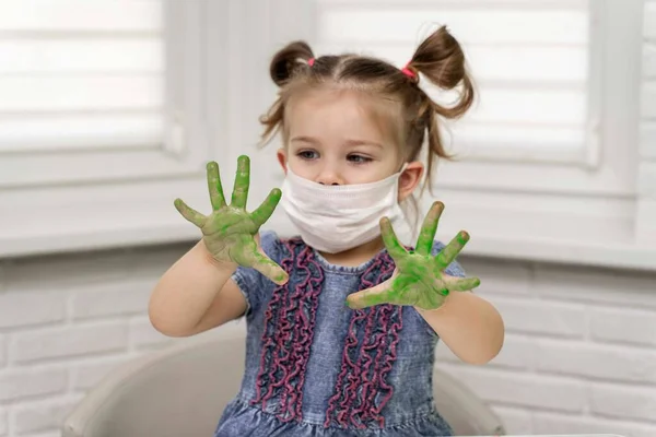 Little girl in mask paints with fingers