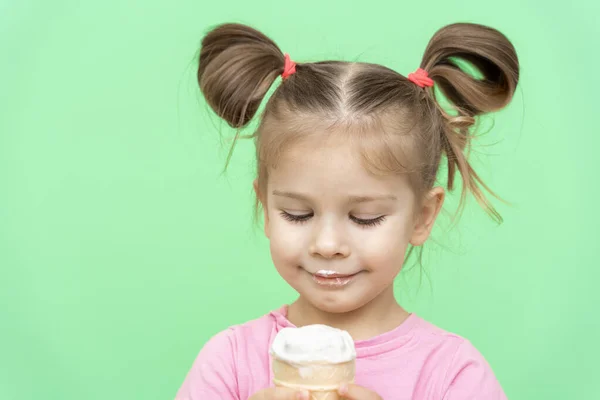 little girl 4 years old in a pink T-shirt on a green background looking at ice cream with pleasure, lips stained with ice cream