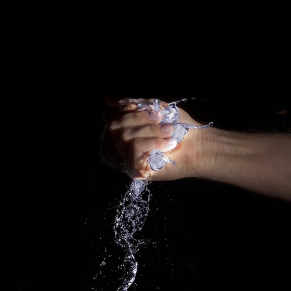 Mano sosteniendo agua azul brillante sobre fondo negro — Foto de Stock