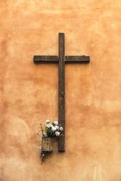 Stary drewniany krzyż chrześcijański na ścianie ozdobione kwiatami — Zdjęcie stockowe