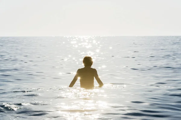 Adolescente niño bañándose en el mar rodeado por el reflejo del rayo de sol —  Fotos de Stock