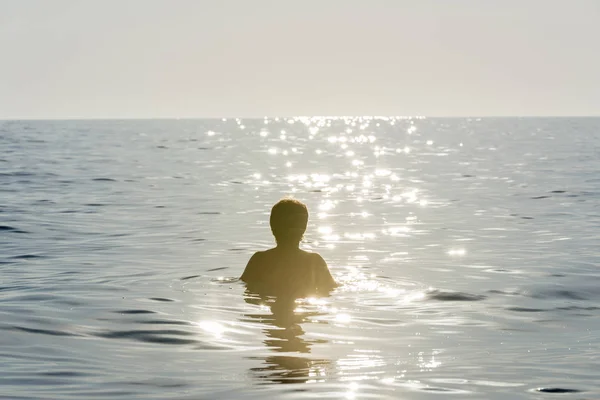 Adolescente niño bañándose en el mar rodeado por el reflejo del rayo de sol —  Fotos de Stock
