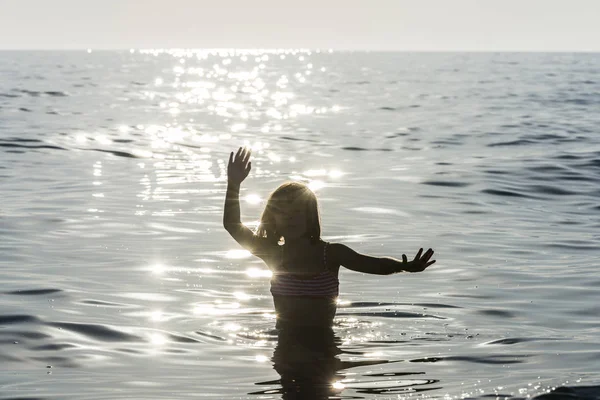 Niña bañándose en el mar rodeada de reflejos de rayos de sol — Foto de Stock