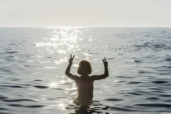 Niña bañándose en el mar haciendo la señal de victoria —  Fotos de Stock