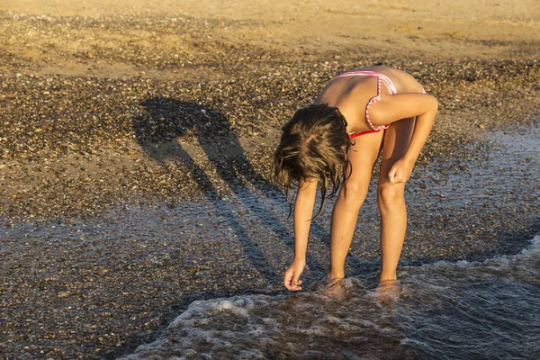 蹲在海滩的小女孩采摘软体动物贝壳 — 图库照片