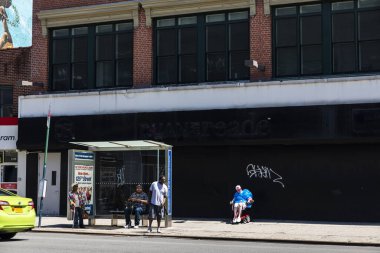 New York City, USA - August 4, 2018: Bus stop on a street with people waiting in Harlem, Manhattan, New York City, USA