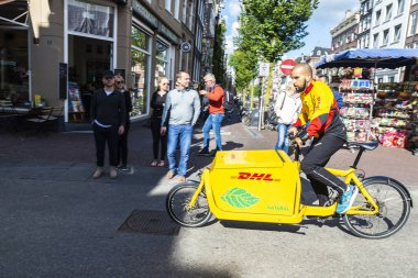 Amsterdam, Hollanda - 7 Eylül 2018: DHL bisikletli genç adam dolaşımı ve Hollanda 'nın Amsterdam kentinin eski tarihi merkezinde yürüyen insanlar