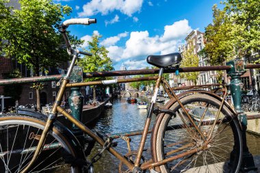 Hollanda, Amsterdam 'da bir kanalın köprüsüne park edilmiş paslı eski bir bisiklet.