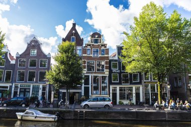Amsterdam, Hollanda - 7 Eylül 2018: Hollanda 'nın eski Amsterdam kentinde yaşayan insanların bulunduğu bir kanal boyunca eski geleneksel eğimli evler