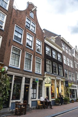 Amsterdam, Hollanda - 8 Eylül 2018: Hollanda 'nın eski Amsterdam kentindeki bir barın terasında kitap okuyan bir adamla alışveriş caddesi