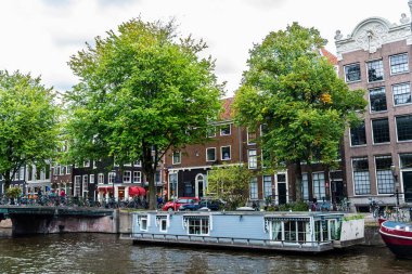 Amsterdam, Hollanda - 8 Eylül 2018: Hollanda, Amsterdam 'daki insanlarla dolu bir kanal boyunca demirlemiş yüzen ev