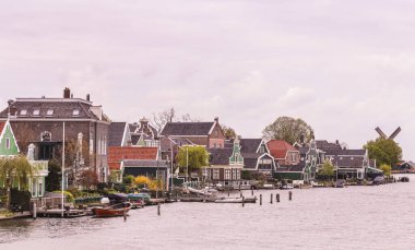 Günbatımı, klasik evler ve yel değirmenleri olan bir nehirde pembe bir kasaba aydınlatıyor.