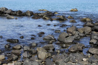 Etrafı mavi okyanusla çevrili küçük kayalar, bazı kayalar zapt edilmiş, ıslak ve bazı kuru kayalar