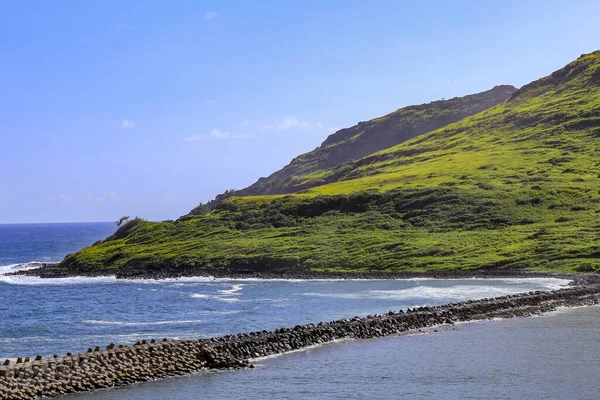 Okyanusta yuvarlanan yeşil tepe ve mavi gökyüzü ile insan yapımı kaya duvar. Kopyalamak için boşluk