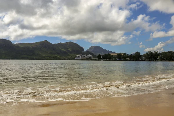 Bulutlu bir günde kumlu sahilde küçük bir dalga Dağlar ve uzakta küçük bir kasaba
