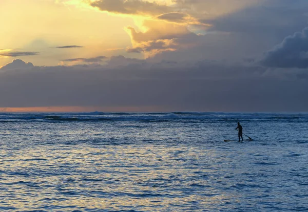 Resmin sağındaki tek kürekçi alçak bulutlar ve bulutların üstünde parlak güneş, gün batımında okyanusta dalgalanmalar.