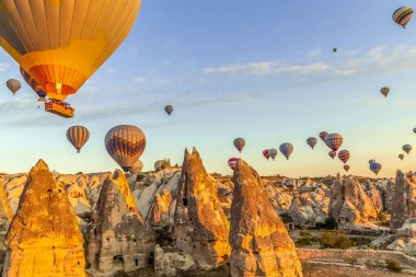 Açık gökyüzünde, Cappadocia 'daki vadi ve evlerin hemen üstünde bir sürü sıcak hava balonu yüzüyor.