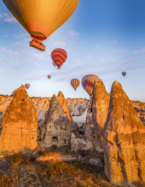 Cappodocia 'daki mağara evlerinin hemen üstünde yüzen renkli balonlarla parlak sarı gündoğumu