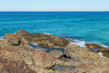 Büyük kayalarla dolu kıyı şeridi küçük kaya havuzları oluşturuyor, yoğun mavi okyanus küçük dalgalar yaratıyor.