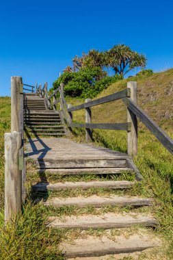 Parlak bulutsuz gökyüzü ile tepeyi tırmanan çimenli kum ahşap merdivenler.