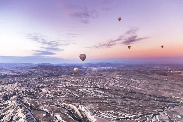 Purple sunrise with several hot air balloons floating above the valleys in Nevsehir, Cappadocia, Turkey