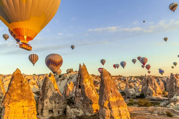 Açık gökyüzünde, Cappadocia 'daki vadi ve evlerin hemen üstünde bir sürü sıcak hava balonu yüzüyor.