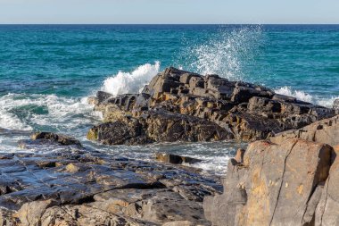 Kırık dalgalı kayalar güneşli bir öğleden sonra deniz spreyi püskürtüyor.