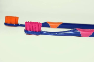 Beyaz arka planda diş macunlu iki diş fırçası. Diş fırçasının üzerindeki diş macunu beyaza izole edilmiş. Pembe diş fırçası. Turuncu diş fırçası