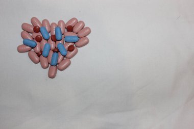 Mavi ve kahverengi haplardan yapılmış bir kalp. Farklı renkli tabletlerden yapılmış kalp beyaza izole edilmiş. Metin için kopyalanma alanı. Salgın, ağrı kesiciler, sağlık, tedavi hapları ve bağımlılık konsepti.