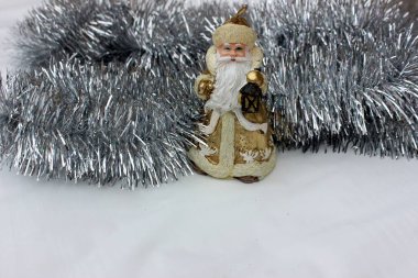 Gümüş arka planda Noel Baba 'nın heykeli. Altın Noel Baba mumu beyazın üzerinde izole edilmiş. Bej renkli Aziz Nicholas. Altında yazı için bir yer var. Noel ağacını süslemek için gri yağmur.