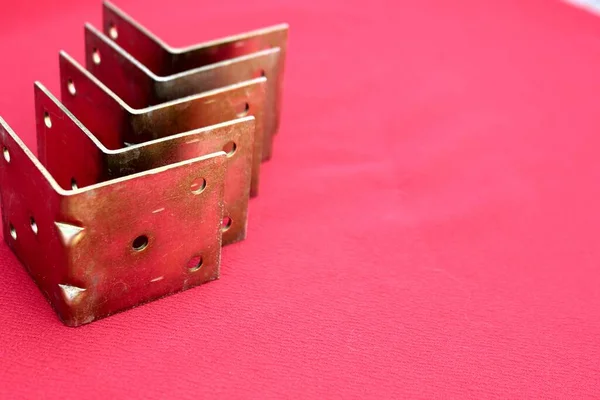Arrow made of brackets isolated on pink. Metal corners pointing down with a place for the text. Golden metal bracket on a red background. Metal corners frames, borders. Isolated.