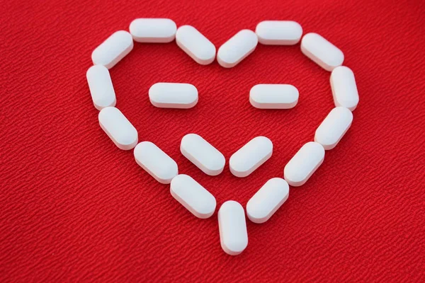 Heart made of white pills isolated on red background. Face in heart made of pills. Medicine concept.